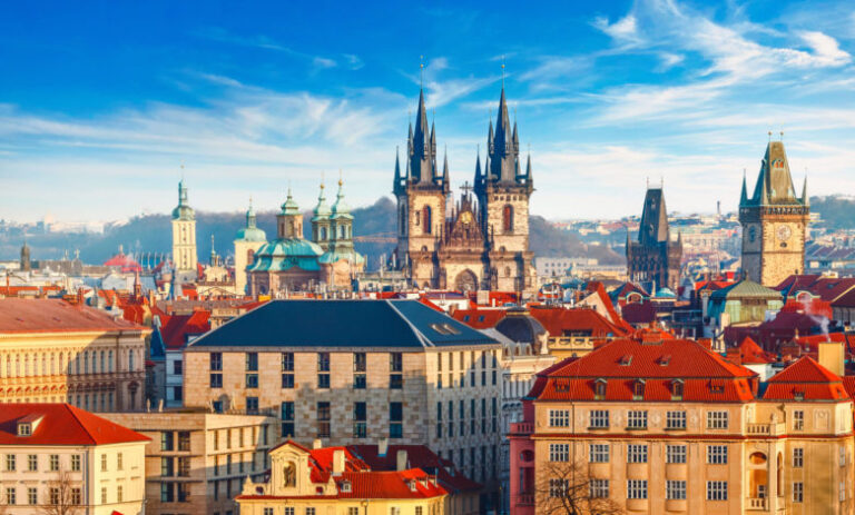 High spires towers of Tyn church in Prague city (Church of Our Lady before tyn cathedral) urban landscape panorama with red roofs of houses in old town and blue sky with clouds